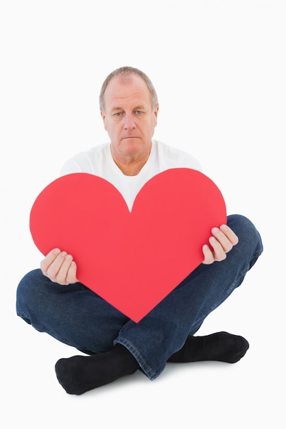 Upset man sitting holding heart shape