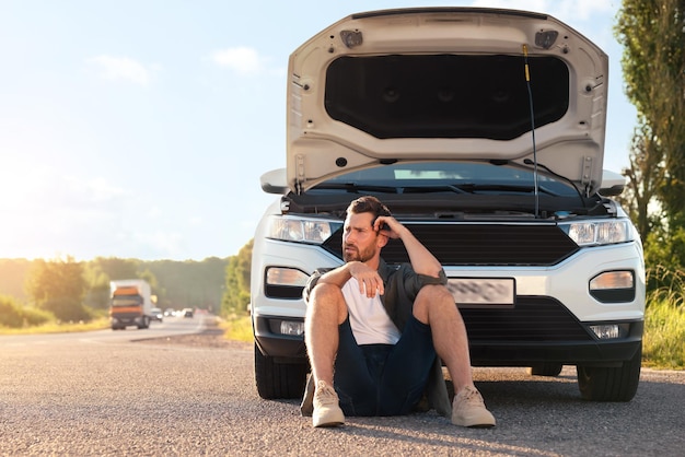 道端で壊れた車の近くに座っている動した男