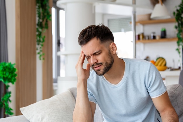 Upset man squeezing head with hands writhing in pain suffering from headache at home copy space