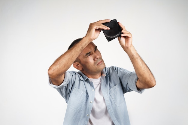 Upset mature man holding and looking inside his empty wallet on white background. financial crisis, bankruptcy, no money, bad economy Concept.