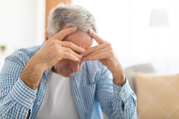 Upset mature man sitting on couch and thinking