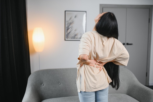 Upset mature woman suffering from backache unhappy senior blonde sitting on a sofa at living room feeling discomfort because of pain in back