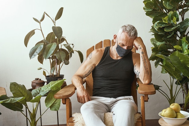 Upset middle aged caucasian man wearing protective face mask during coronavirus pandemic sitting on