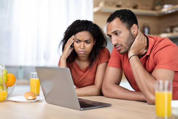 Photo upset millennial black wife and husband have video call look at laptop in minimalist kitchen interior