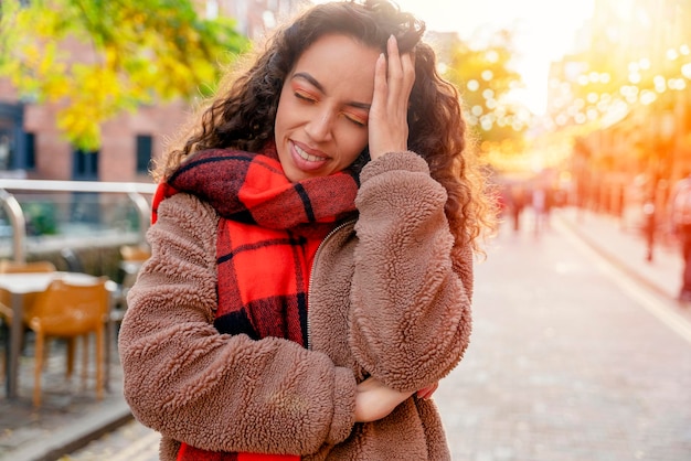 Photo upset mixed race woman in brown coat and orange scarf walking outdoors in celebrating city