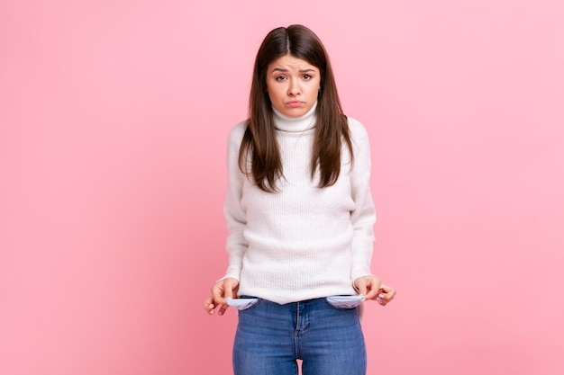 Upset poor girl showing empty pockets and looking frustrated about loans and debts has no money