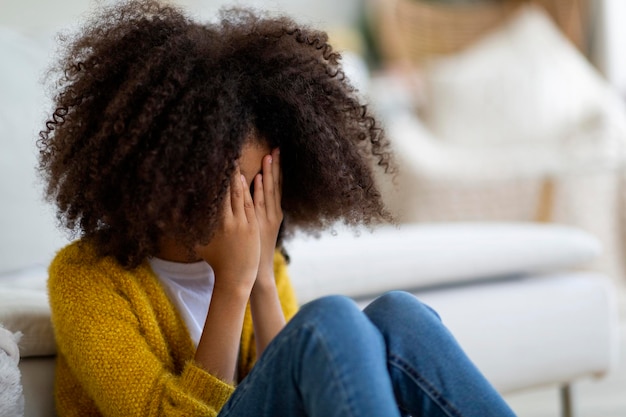 Upset preteen black girl sitting on floor at home crying