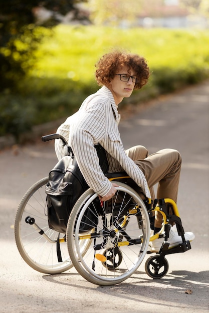 Upset redhaired guy in glasses sits in a wheelchair Sad man looking at camera outdoors