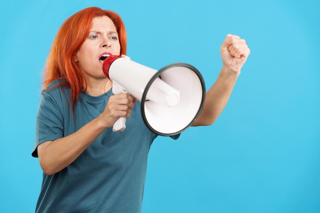 Upset redheaded mature woman yelling using a loudspeaker