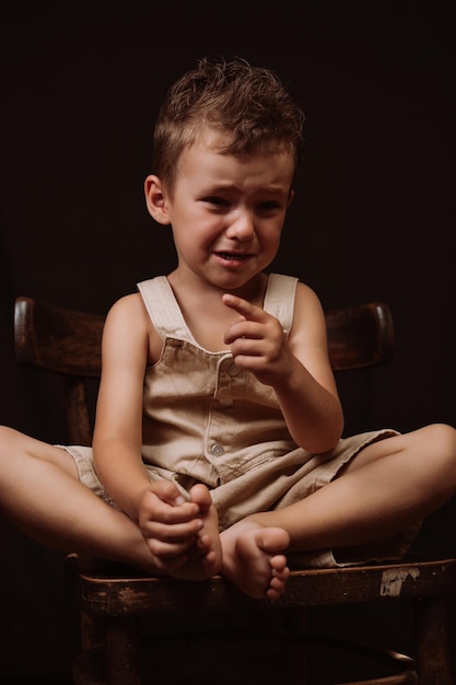 Upset sad caucasian boy crying sitting on a wooden chair