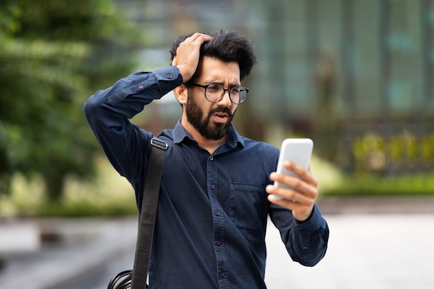 Upset sad eastern businessman reading bad news online on phone