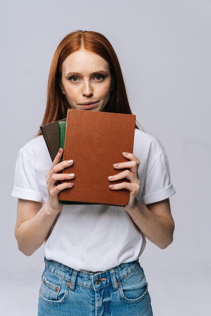 Upset sad young woman college student holding book and looking at camera on isolated gray background Pretty redhead lady model wearing casual fashion clothes emotionally showing facial expressions