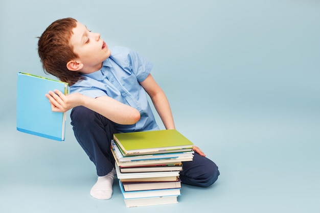 Upset schoolboy sitting with pile of school books and throwing a textbook