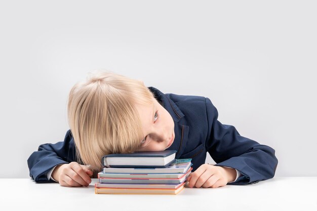 Upset schoolboy with pile of school books and notebooks Tired or bored boy sleeps at the table