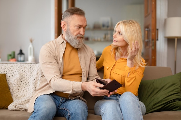 Upset senior husband showing empty wallet to wife at home