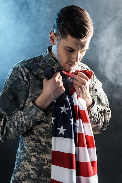 Upset soldier holding american flag on black with smoke