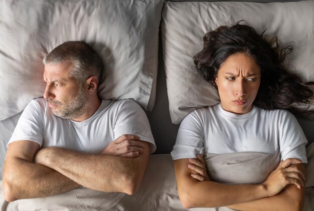 喧の後 動した夫婦 毛布の下でベッドに横たわり 腕を交わして 互いを無視する男と女