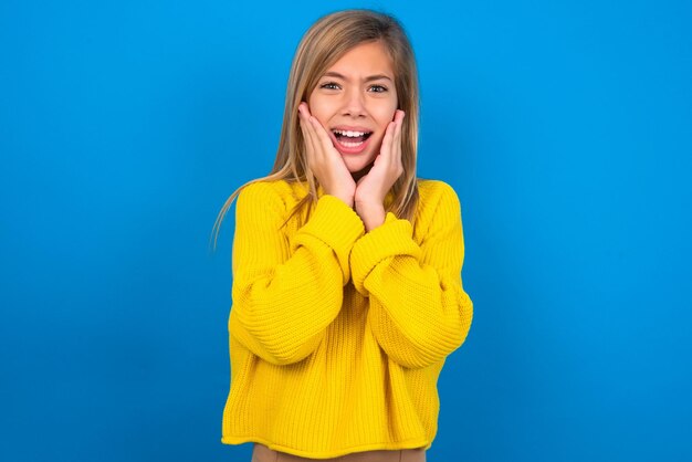 Upset teen girl wearing yellow sweater touching face with two hands