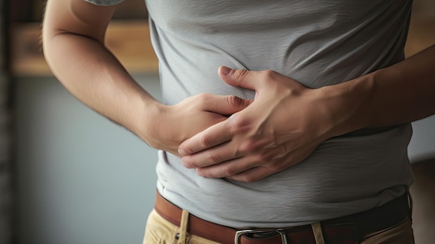 Upset unhappy young man holding his abdomen with both hands suffering from bellyache isolated on gray background