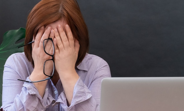 Donna turbata ha chiuso il viso delle mani vicino al suo posto di lavoro con il laptop