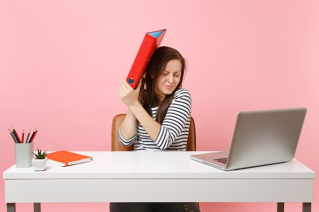 Upset woman defending hiding behind red folder with paper document work on project while sit at office with laptop 