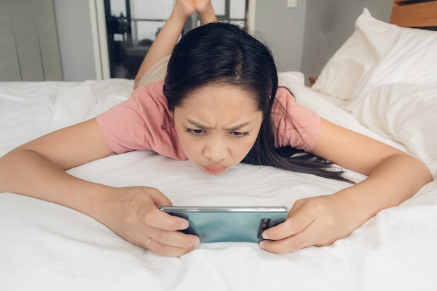 Upset woman is playing mobile game on her bed.