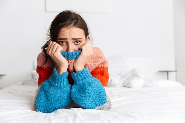 upset woman looking at camera and crying, while lying on bed in apartment