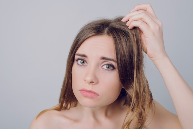 Upset woman looking her damaged hair on gray