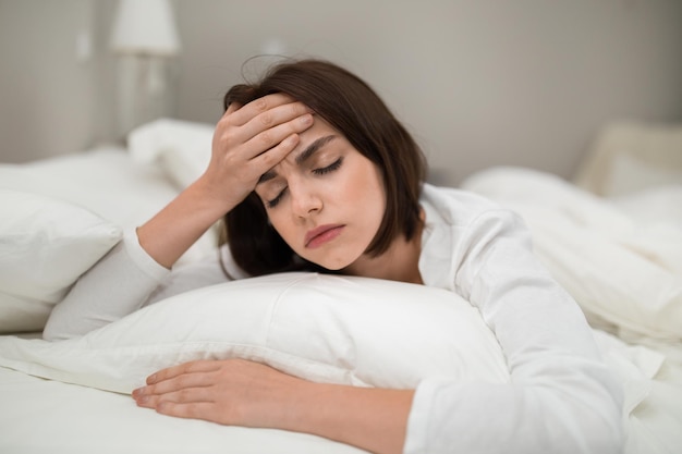 Upset woman lying in bed at home touching head