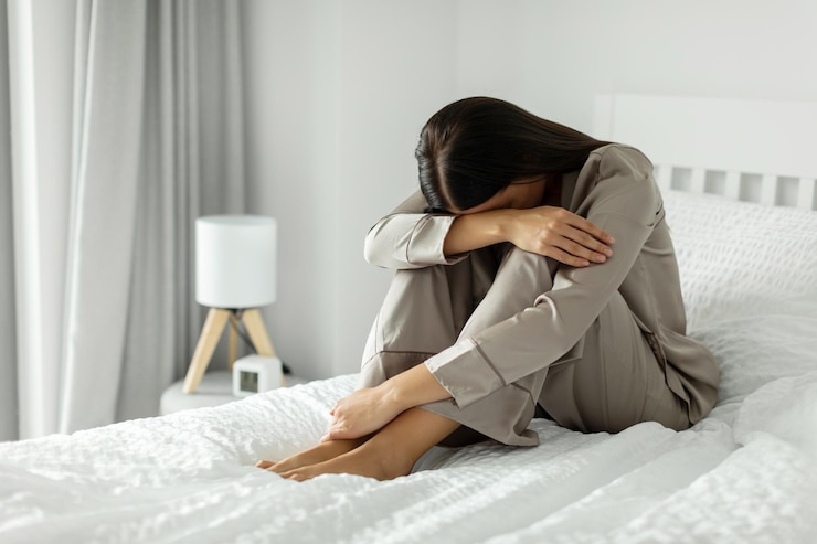 Photo upset woman in pajamas sitting on bed at home embracing her knees and crying having bad days