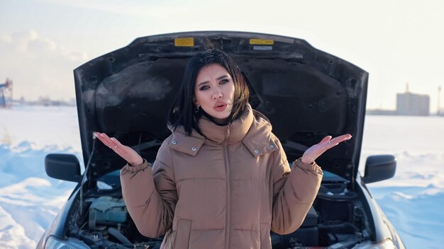 Upset woman shrugs standing near broken automobile in field