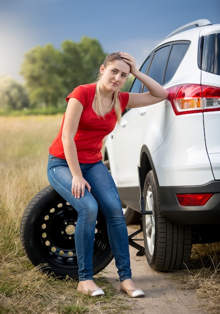 Upset woman sitting next to broken car at field