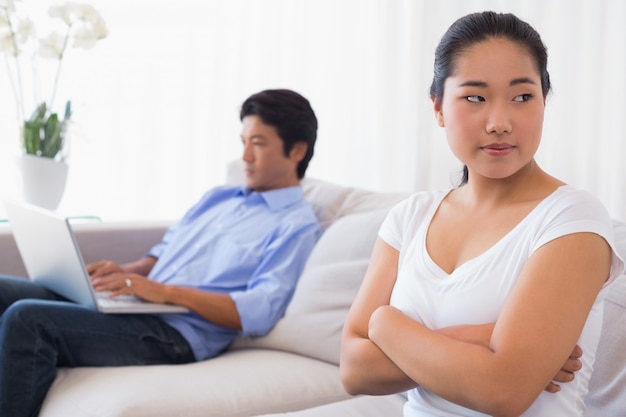 Upset woman sitting on couch while boyfriend uses laptop at home in the living room