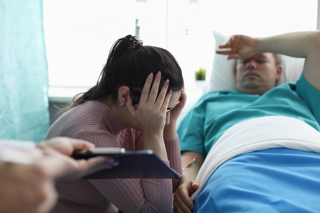 Upset woman sitting near man in hospital bed