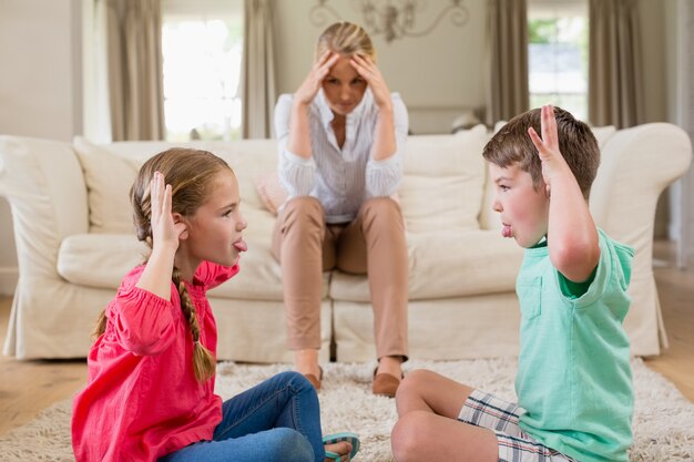 Upset woman sitting on sofa while siblings teasing each other