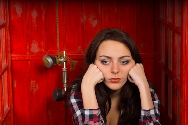 Upset woman sitting with the phone off the hook to block the line as a vintage handset dangles alongside her head