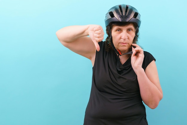 An upset woman wearing a bicycle helmet shows his thumb down on\
a blue background insurance injury protect secure protective\
perfect cycle express accident guard hobbies tool protector