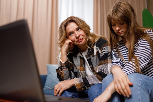 Donne sconvolte di età diverse sedute sul divano in soggiorno guardando il computer portatile