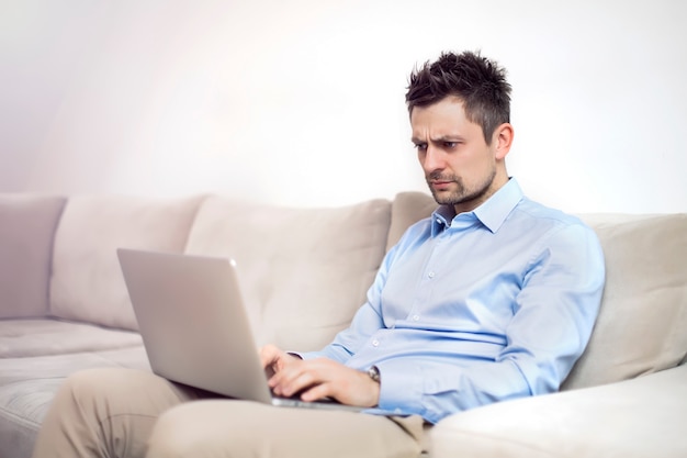 Upset and worried young businessman sitting and working at laptop