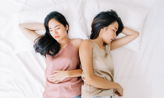 Upset young Asian lesbian couple having a disagreement lying side by side in bed