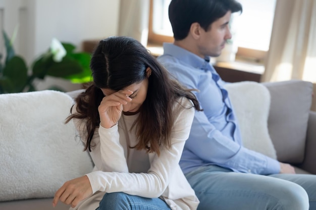 Photo upset young caucasian couple sit on sofa back to back think of divorce or breakup after family fight unhappy man and woman avoid talking having relationships problems spouse split concept