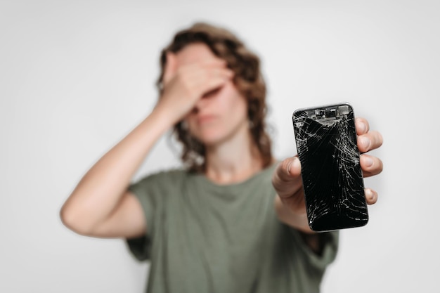 Upset young woman holding her broken smartphone. Phone screen need to repair. isolated on gray background.