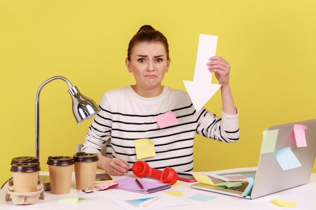 Upset young woman showing white arrow pointing down expressing negative emotions