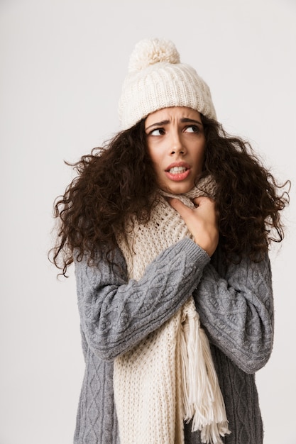 Upset young woman wearing winter scarf standing isolated over white wall, shivering