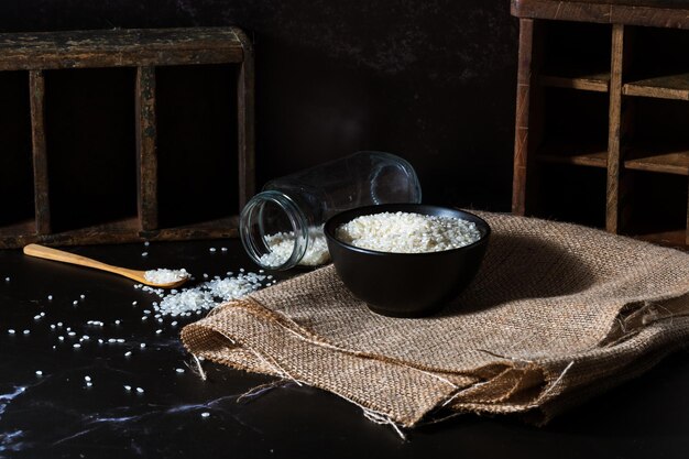 Upside down jar wooden spoon and black bowl with raw white yamani rice