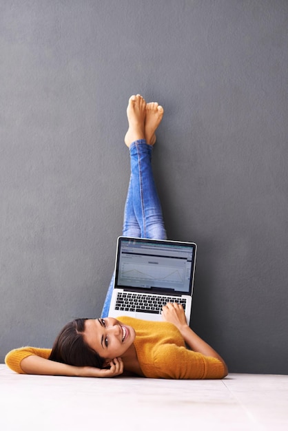 Преимущество технологий Молодая женщина лежит на полу с ноутбуком на сером фоне