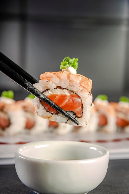 Uramaki blowtorcherd salmon on chopsticks with soy sauce. Closeup.