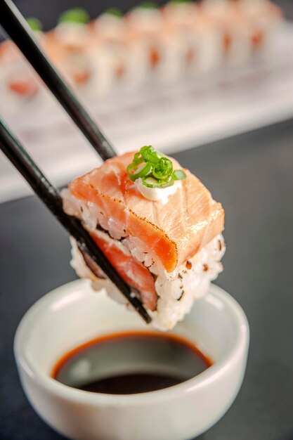 Uramaki blowtorcherd salmon on chopsticks with soy sauce. Closeup.