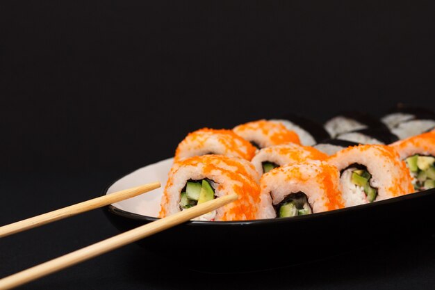 Uramaki Californië. Sushibroodjes met nori, rijst, stukjes avocado, komkommer, versierd met vliegende viskuit op keramische plaat met houten stokjes.