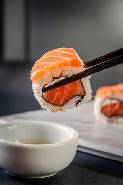 Uramaki salmon on chopsticks with soy sauce. Closeup.